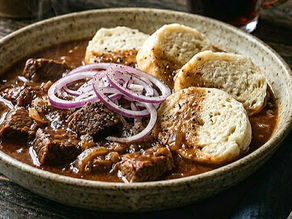 Hearty stew with beef chunks and red onion slices, served with dumplings in a rustic bowl on a wooden table. Warm, cozy setting.