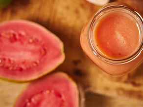 Top view of a jar filled with pink smoothie beside halved pink guavas on a wooden surface. Bright colors and fresh, tropical vibe.