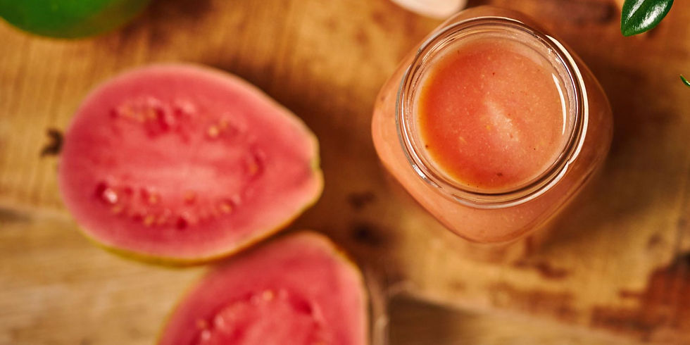 Top view of a jar filled with pink smoothie beside halved pink guavas on a wooden surface. Bright colors and fresh, tropical vibe.