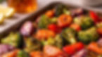 Roasted vegetables in a tray, featuring broccoli, carrots, red bell peppers, and onions. Bright colors and a rustic kitchen setting.