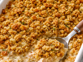 Golden-brown breadcrumb-topped casserole with creamy chicken is served in a white dish. A spoon is scooping a portion.