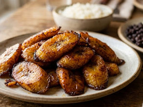 Plate of caramelized fried plantains on a rustic wooden table, with bowls of rice and black beans in the background.