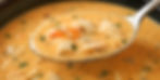 Spoon of creamy seafood bisque with chunks of crab and shrimp, garnished with green herbs, in a bowl. Warm and savory ambiance.