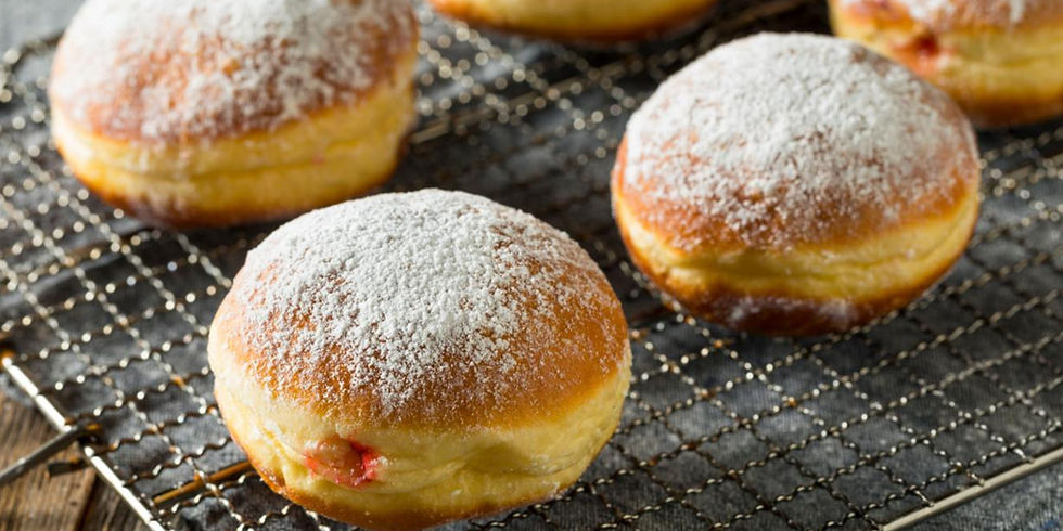 Powdered sugar-covered jelly donuts on a cooling rack, wooden table beneath. Warm lighting enhances their golden-brown color.