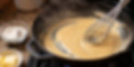 Freshly made blonde roux cooking in a cast-iron skillet, showing silky whisk trails and a light golden color with flour and butter ingredients beside the stove.