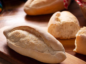 Freshly baked bread rolls on a wooden board, with a basket and colorful cloth in the background, creating a warm, rustic feel.