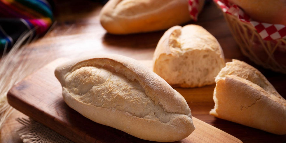 Freshly baked bread rolls on a wooden board, with a basket and colorful cloth in the background, creating a warm, rustic feel.