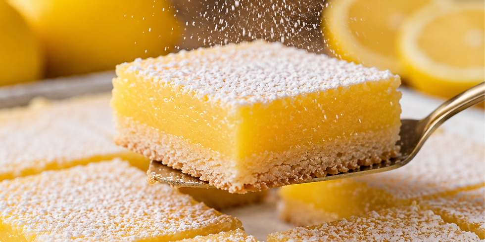 Lemon bar with powdered sugar dusting on top, held by a spatula. Fresh lemons in background. Bright, inviting, and delicious.
