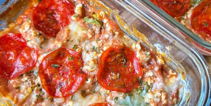 A glass baking dish with baked cottage cheese topped with melted cheese and pepperoni slices, garnished with herbs, creating a savory and appetizing look.