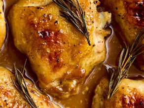Golden brown roasted chicken thighs with crispy skin and sprigs of rosemary in savory sauce. Close-up shot emphasizes texture.