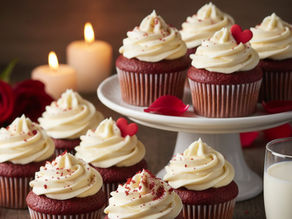 Red velvet cupcakes with cream frosting and heart toppers on a white stand. Background: lit candles, red rose petals, glass of milk.