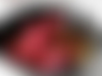 Chunks of raw beef marinating in a dark liquid with herbs and garlic in a black bowl. A spoon is visible. The setting is a light wooden surface.