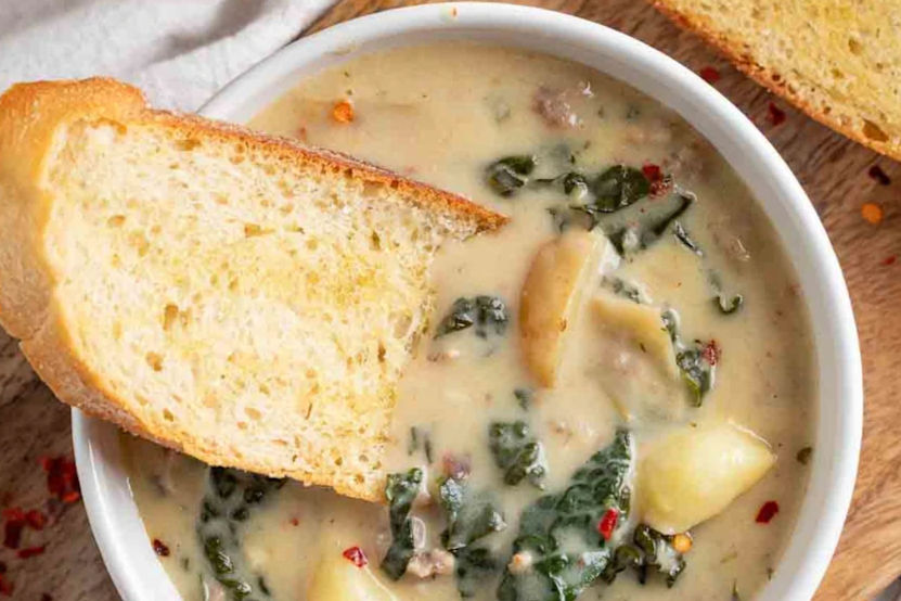 A bowl of creamy soup with spinach and potatoes, topped with a slice of toasted bread on a wooden table. Cozy and inviting atmosphere.