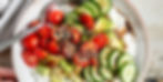 Bowl of cottage cheese topped with cherry tomatoes, cucumber slices, avocado, and seeds, drizzled with balsamic glaze. Bright, fresh colors.