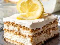 Slice of Lemon Icebox Cake topped with whipped cream and fresh lemon slices, showing creamy lemon layers.