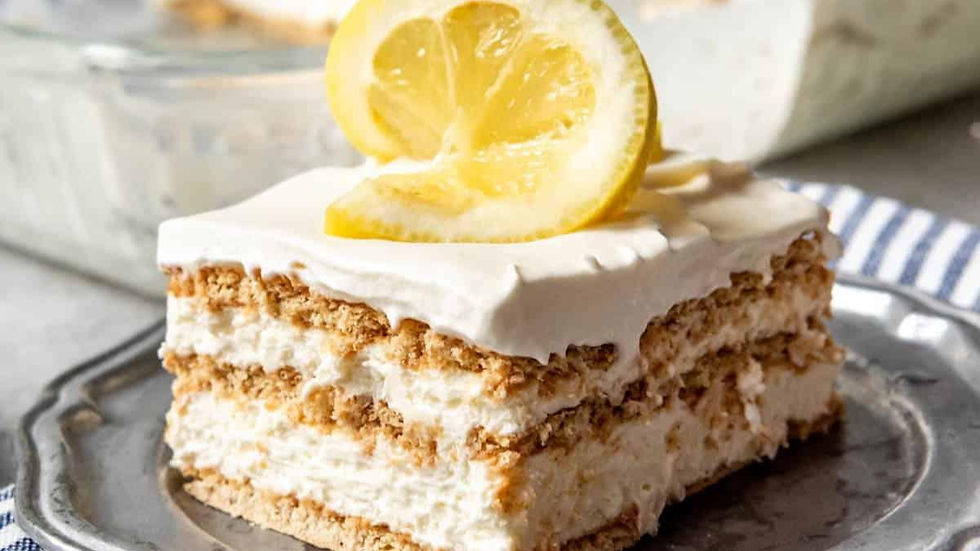 Slice of lemon icebox cake on a silver plate topped with lemon slices. Creamy layers, graham crackers, with a striped cloth in view.