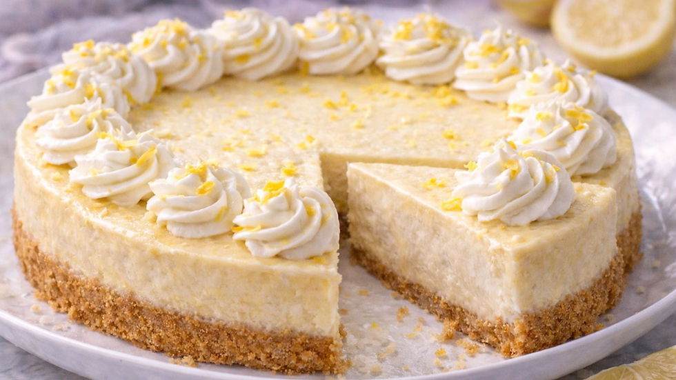 Creamy cheesecake with a graham crust topped with whipped cream and lemon zest. A slice is removed, revealing a smooth texture.