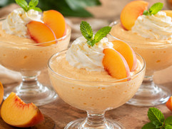 Light and creamy peach mousse served in elegant dessert glasses, garnished with whipped cream, fresh peach slices, and mint leaves.