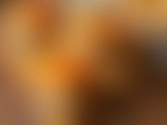 Three cheeseburgers with caramelized onions on a wooden board. Background shows fries and a dip, creating a warm, appetizing scene.