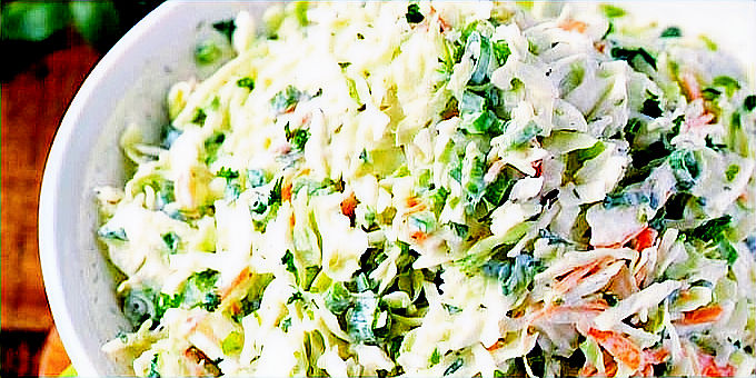 Bowl of creamy coleslaw with cabbage, carrots, and parsley. Vibrant greens and oranges on a wooden table with a green polka dot cloth.