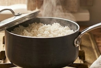 White rice cooking in a saucepan with steam rising during the stovetop simmering process.