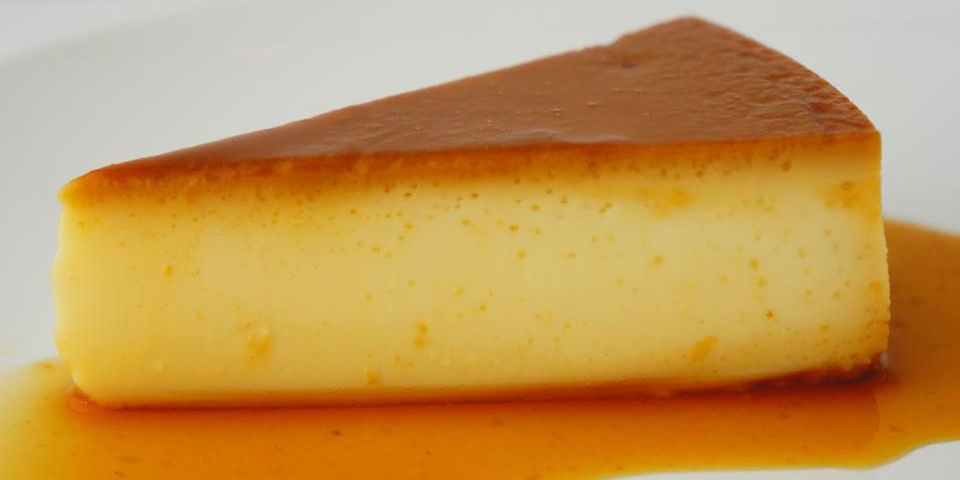 Slice of caramel flan on a white plate, with a rich caramel topping and syrup pooled around. Bright and smooth texture.
