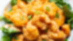 Fried shrimp coated in a creamy orange sauce are placed on green lettuce leaves, garnished with chopped green onions.
