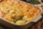Golden cheesy potato gratin in a baking dish on a rustic wooden table, with a slice missing. Sour cream and herbs in the background.