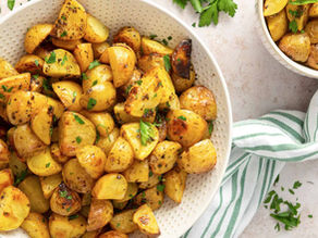 Roasted potatoes with herbs in a white bowl on a light surface. A green-striped cloth is beside the bowl, creating a cozy, inviting mood.