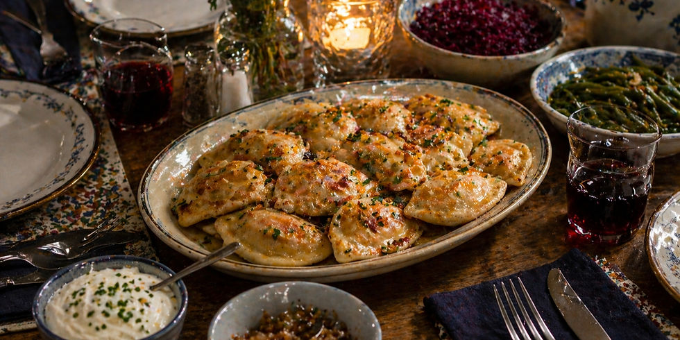 A cozy dinner table with a platter of golden pierogies, drinks, and sides like green beans and red cabbage. Warm, inviting ambiance.