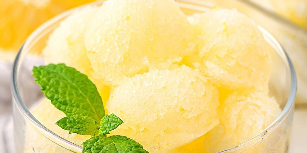 Yellow lemon sorbet scoops in a glass bowl with a fresh mint garnish, set against a softly blurred yellow and white background.