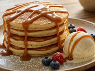Stack of fluffy pancakes drizzled with dulce de leche and served with fresh berries and whipped cream.
