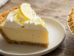 Slice of coconut cream pie with a flaky crust and whipped cream topping, garnished with lemon slices and served on a white dessert plate.