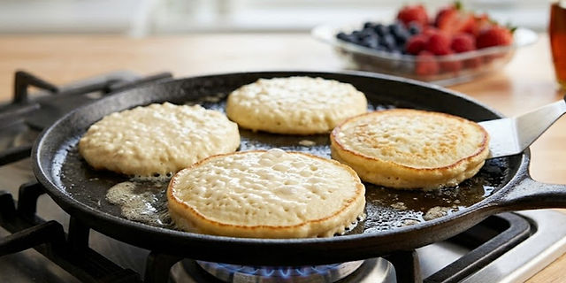 Cottage cheese pancakes cooking in a lightly buttered skillet as bubbles form on the surface, showing they're ready to flip.