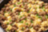 Scrambled eggs mixed with browned sausage and green onions in a black skillet. The dish has a savory and appetizing appearance.