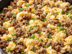 Scrambled eggs mixed with browned sausage and green onions in a black skillet. The dish has a savory and appetizing appearance.