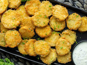 Golden fried zucchini slices garnished with parsley on a dark plate, served with a side of creamy dipping sauce.