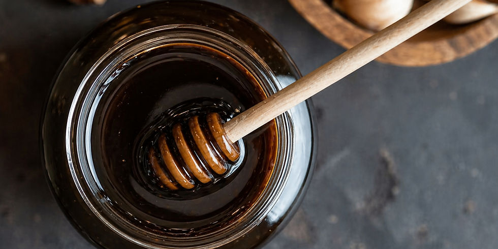 A jar of dark honey with a wooden honey dipper submerged inside, set on a textured dark surface, creating a rich, natural atmosphere.