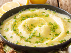 Creamy dip in a black bowl, garnished with green onions, on a wooden table. Lemon slices and walnuts are nearby. Cozy, rustic setting.