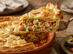 Traditional Venezuelan Polvorosa de Pollo with a flaky golden crust and savory chicken filling, served in a rustic baking dish with one slice removed.