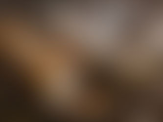 Baguette and glass jar of spread on a wooden board, surrounded by garlic cloves and a wooden spoon, on a rustic table.