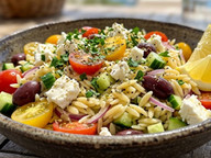 Greek orzo salad with cucumbers, tomatoes, Kalamata olives, feta cheese, and fresh herbs in a rustic bowl.