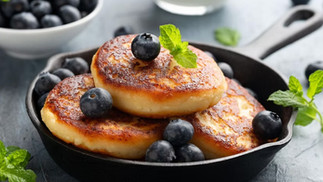 Stack of golden cottage cheese pancakes topped with fresh blueberries and mint, served warm in a cast-iron skillet.