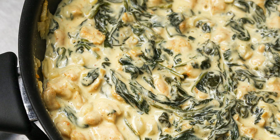Creamy chicken and spinach dish cooking in a black skillet. The sauce is rich and golden with green spinach leaves visible throughout.