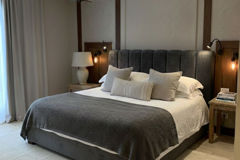 A luxurious double bed in a custom-made design with a high headboard upholstered in a distribution of puffy strips in a charcoal graphite shade.