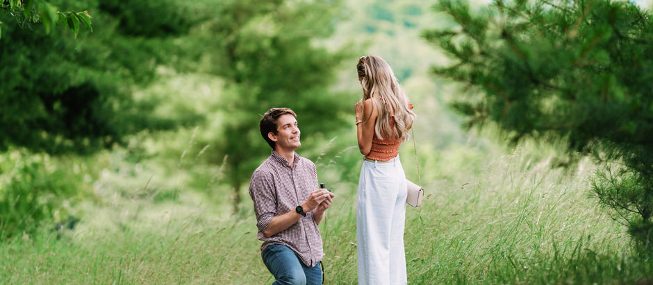 Man on one knee proposing to his girlfriend in a green grassy field 