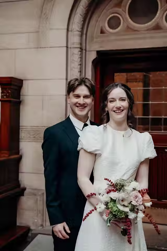 Close-up portrait of the bride and groom standing together at Copenhagen City Hall, smiling with the bride holding her bouquet.