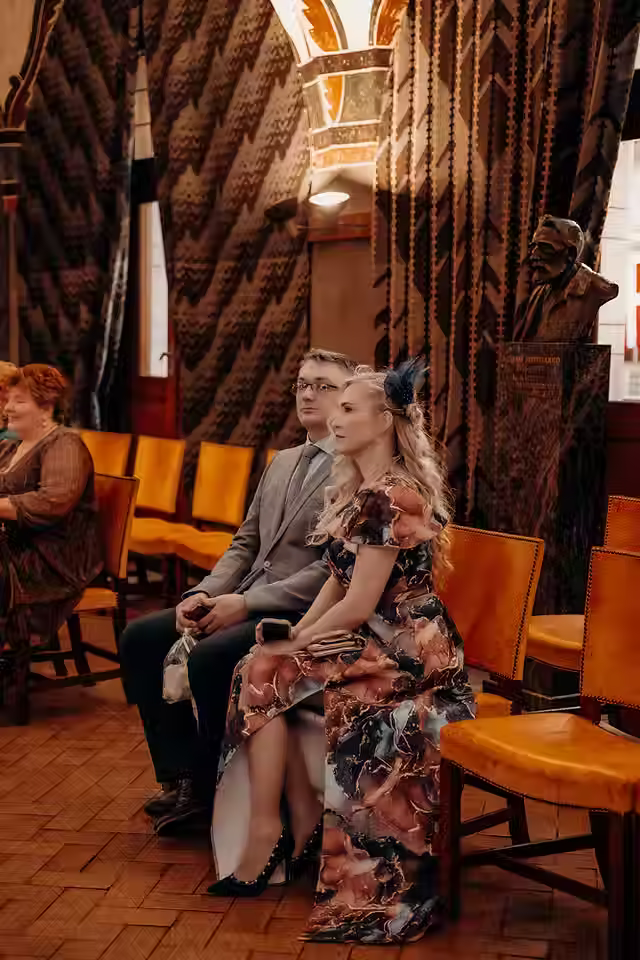 Wedding ceremony inside Copenhagen City Hall’s mural room with the officiant reading and the couple standing before detailed wall paintings.