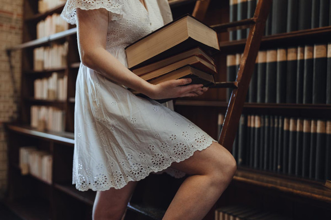 Woman in white dress browsing books in warm library light