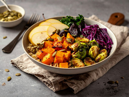 Grain bowl with roasted delicata squash, Brussels sprouts, beets, kale, red cabbage, fresh pear slices, and pumpkin seeds served on quinoa in a ceramic bowl.